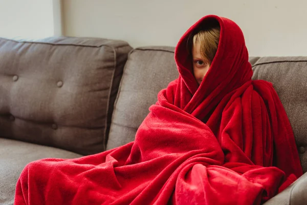 Konfor ve sıcaklık için Robicheaux kırmızı battaniye ile bir kanepede oturan 8 yaşında bir çocuk