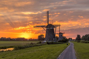 Hollandalı polder peyzaj turuncu günbatımı altında iki tarihi ahşap yel değirmenleri