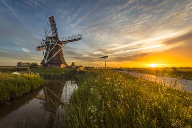 Hollanda ahşap Yeldeğirmeni kanal günbatımı pistte çiçek ve güzel gökyüzü yaz alanında Bisiklete binme