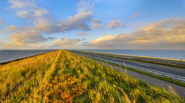 Afsluitdijk Hollandalı dike otoyol ve parça bulutlu gökyüzü günbatımı sırasında Bisiklete binme