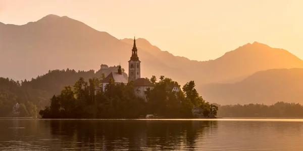 Ön med kyrkan i sjön Bled på orange disig morgon — Stockfoto