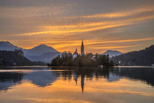 Krajobraz jezioro Bled z kościołem pod pomarańczowy rano niebo — Zdjęcie stockowe