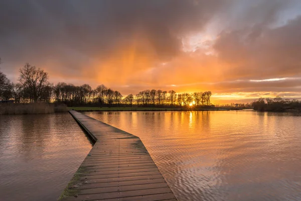 オレンジ色の夕日の下の湖に木製の通路 — ストック写真