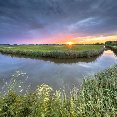 Hollanda 'nın Groningen bölgesindeki düz tarım arazisinde gün batımında nehir kıvrımları üzerinde geniş açı manzarası.