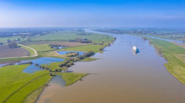Hollanda, Gelderland 'deki Ravenswaaij köyü yakınlarındaki River Lek hava manzaralı konteynır mavnası.