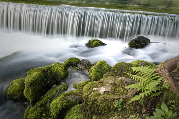 コケに覆われた岩の背景を持つ美しい滝 — ストック写真