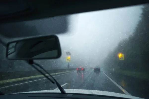 Dangerous blurry driving car in the rainy and slippery highway. Rain through windshield of moving vehicle. Personal perspective used.