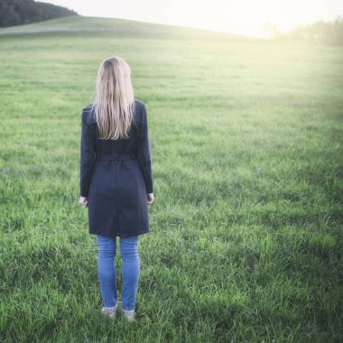 Arkadan güneşli çayır üzerinde duran sarışın model kadın görünüşü. Kullanılan renk filtre efekti.