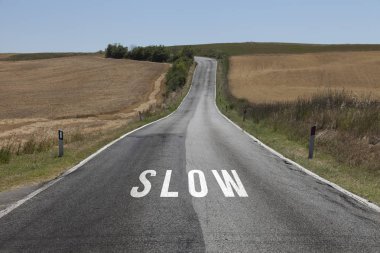 Concept drive slow message on the sunny summer asphalt country road. Conceptual slowly driving alert background.