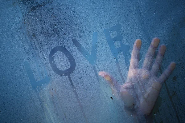 Lonely person in love standing by the window and touching the wet glass with his hand. Selective focus used.