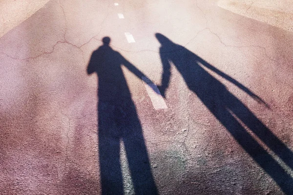 Shadow of man and woman holding hands on walk on city street. Concept broken love background.