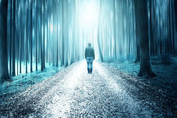 Man standing in artistic blurry surreal forest landscape. Blue color tone effect used.