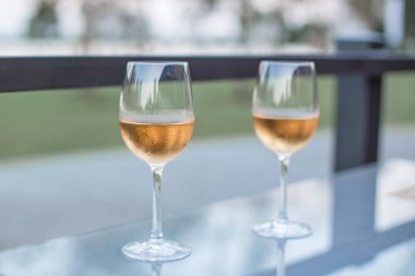 Günbatımı arka planında masanın üzerinde iki bardak pembe şarap. Bir bardak pembe şarap yakın..