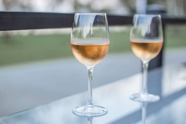 Günbatımı arka planında masanın üzerinde iki bardak pembe şarap. Bir bardak pembe şarap yakın..