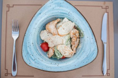 Mavi tabakta tavuklu Sezar Salatası. Teras kafedeki masada ızgara tavuklu Sezar Salatası. Izgara tavuk göğsü ve tabakta taze salata. Minsk, Belarus.