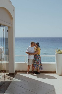 Denize bakan bir balkonda sarılan yaşlı bir çift. Tatildeki bir çiftin fotoğrafı. 80 yaşında..