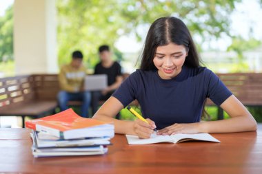 Kız öğrencinin Kütüphane, üniversite kitaplığında atamalar yapıyor masada oturan genç Asyalı kadın adlı bir kitaptan not alma