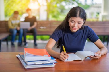 Kız öğrencinin Kütüphane, üniversite kitaplığında atamalar yapıyor masada oturan genç Asyalı kadın adlı bir kitaptan not alma