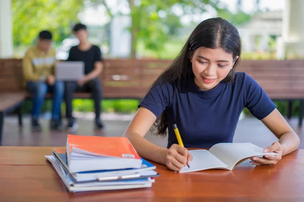 Kız öğrencinin Kütüphane, üniversite kitaplığında atamalar yapıyor masada oturan genç Asyalı kadın adlı bir kitaptan not alma