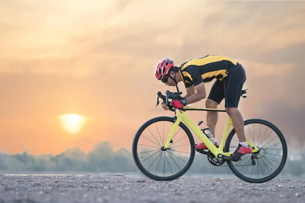 Road bike cyclist man cycling. Biking sports fitness athlete riding bike on an open road to the sunset.