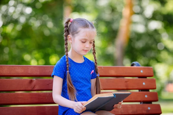 Klein meisje het lezen van een boek buitenshuis. — Stockfoto