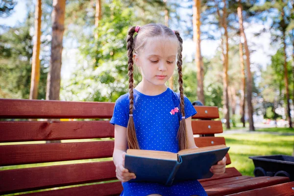 Klein meisje het lezen van een boek buitenshuis. — Stockfoto