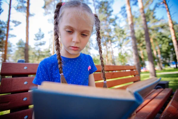 Милая маленькая девочка читает книгу на открытом воздухе — стоковое фото
