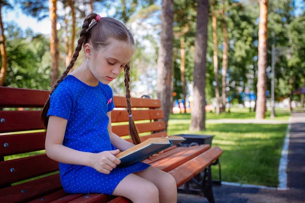 Милая маленькая девочка читает книгу на открытом воздухе — стоковое фото