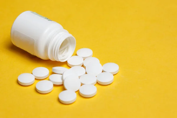 Bílé pilulky linoucí se z bílých plastových prášek láhev na světle žlutém podkladu — Stock fotografie