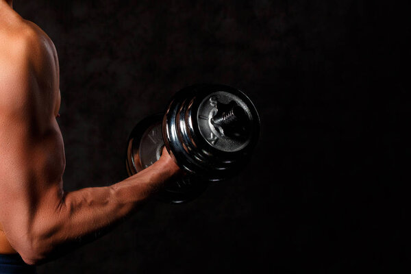 Part of mans body with metal dumbbell on a dark background