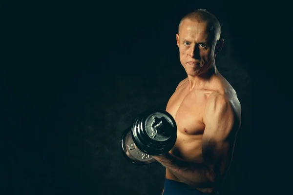 Uomo muscoloso in forma che si esercita con manubri su sfondo scuro. Tonica — Foto Stock