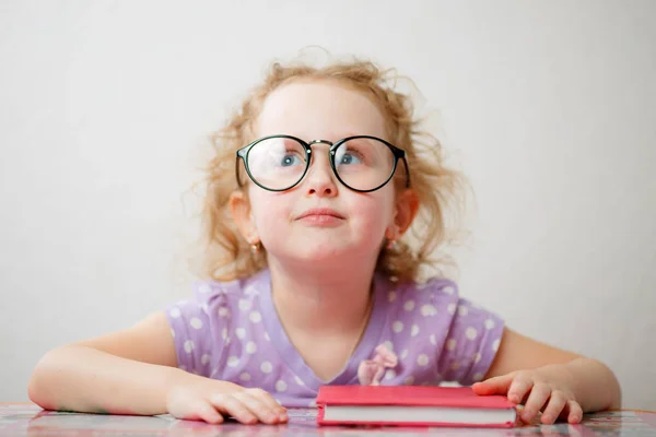 Una niña graciosa con gafas va a leer un libro —  Fotos de Stock