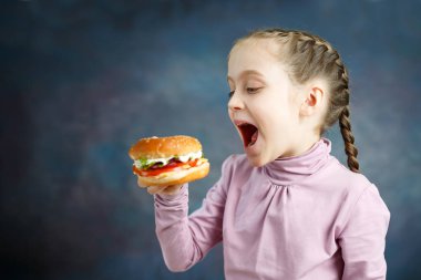 Lezzetli hamburger zevk ile güzel küçük kız mutlu aç anları. Küçük küçük hamburger, yeme kız fastfood - görüntü takip
