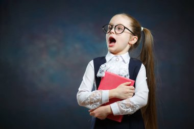 Açık ağız ile beyaz kız öğrenci kitap tut. Suprised İlköğretim Okulu Kız gözlük ve resmi üniforma. Merak yüz ve at kuyruğu saç modeli ile küçük öğrenci portresi