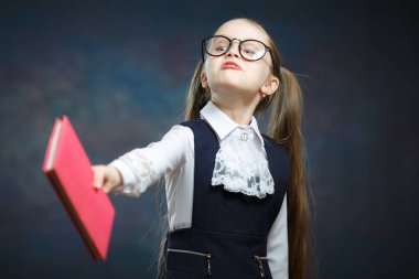 Genç kız öğrenci geçmek basılı kitap Wink tek gözlü. Gözlük kamera açık atış oynak kadın İlköğretim Okulu kız. Koyu arka plan üzerinde uzun at kuyruğu ile küçük çocuk portresi
