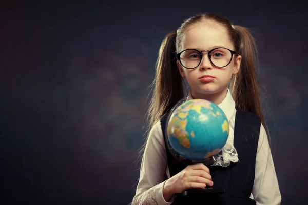 Blonde Little Schoolgirl Hold World Globe in Hand. Female Junior Student Start to Study Geography. Pretty Girl with two Long Ponytail in School Uniform Look at Earth Map Model. Color Tone