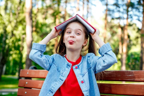 Kind Meisje Met Boek Haar Hoofd Toont Tong Buiten — Stockfoto