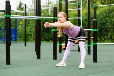 Spor kıyafetli genç bir kadın dışarıda sabah antrenmanı yapıyor. Sportif kız sokak sporları alanında koşmadan önce kaslarını esnetiyor. Formda ve sağlıklı konsept.