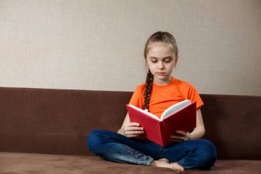 Kid Girl kanepede kitap okuyor. Uzaklık Öğrenme.