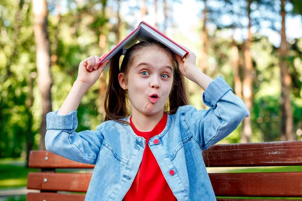 Jovencita Sonriente Alegre Con Libro Cabeza Parque Divirtiéndose Mirando Cámara —  Fotos de Stock