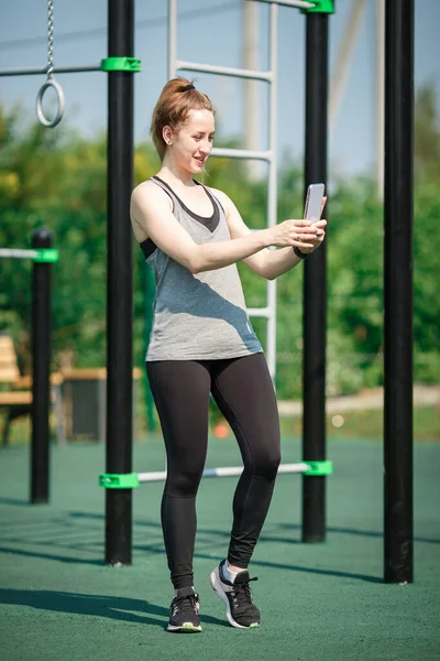 Attractive athletic woman on a street sports field takes a selfie.