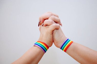Beyaz arka planda gökkuşağı renginde bilekliği olan el işareti yapan bir kadın eşcinsel, lezbiyen, biseksüel ve transseksüel, LGBT sosyal hareketlerin sembolü olan Gay Pride 'ın Kutlaması..