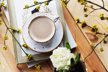 Bir fincan kahve ve sarı çiçekli ahşap zemin üzerine bir kitap. İş yeri. Sıcak bir kahvaltı. Bahar konsepti