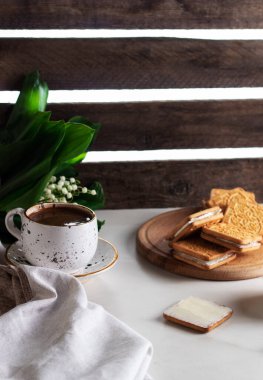 Tereyağı, gevrek kare kurabiyeler ve kahve üzerine yayılmış. Vadi zambakları. Kahvaltı Kompozisyonu