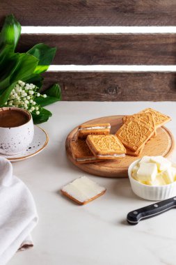 Tereyağı, gevrek kare kurabiyeler ve kahve üzerine yayılmış. Vadi zambakları. Kahvaltı Kompozisyonu