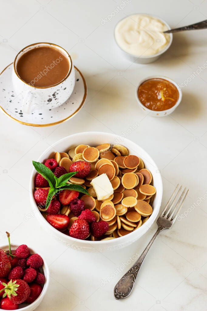 Mini pancake cereal with berry and mint leaves on white background. Sour cream, jam. Trendy Food breakfast Concept.