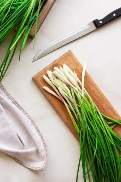 Taze yeşil soğanları beyaz arka planda tahta bir tahtada dilimliyorum..