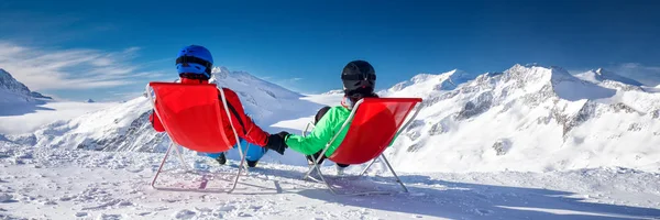 Young couple sitting on deck chairs and enjoying stunning view of Alps, Europe.