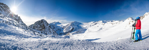 Молодой счастливый лыжник сидит на вершине гор и наслаждается видом на Ретийские Альпы с ледника Пресена, перевал Тонале, Италия, Европа
.  
