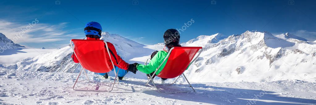 Young couple sitting on deck chairs and enjoying stunning view of Alps, Europe. 